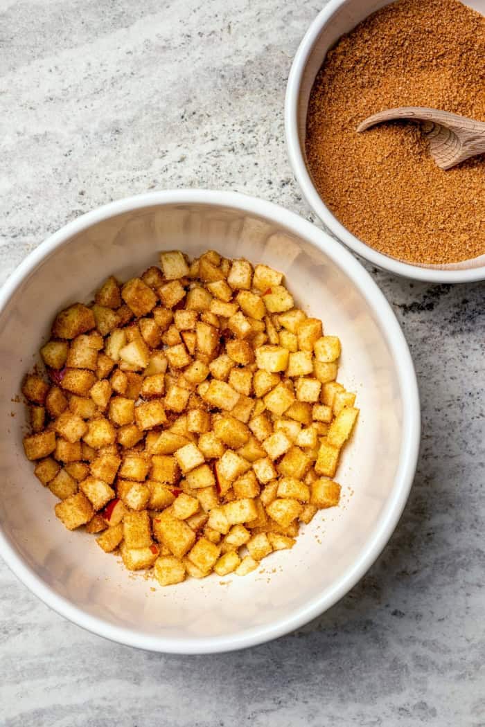 Spiced apples in bowl next to bowl of apple pie spice sugar.