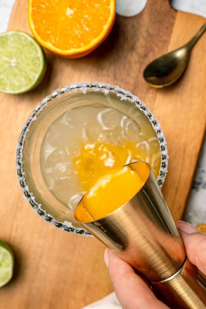 Deliciously tart and refreshing, this fizzy Margarita Mocktail has the bright citrus flavor of the real-deal, in non-alcoholic form! Pouring orange juice into glass with salted rim