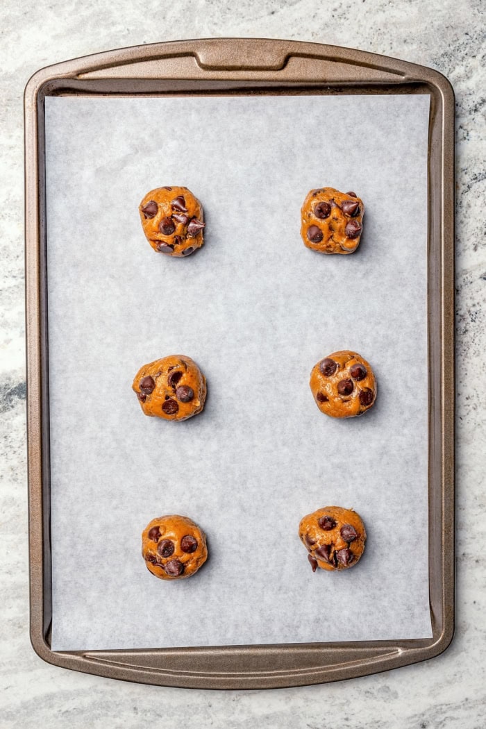 Soft, moist, and chewy, these Pumpkin Chocolate Chip Cookies are the perfect sweet treat for fall! Pumpkin pie spice adds warm, cozy flavor. Balls of dough for pumpkin chocolate chip cookies on baking sheet.