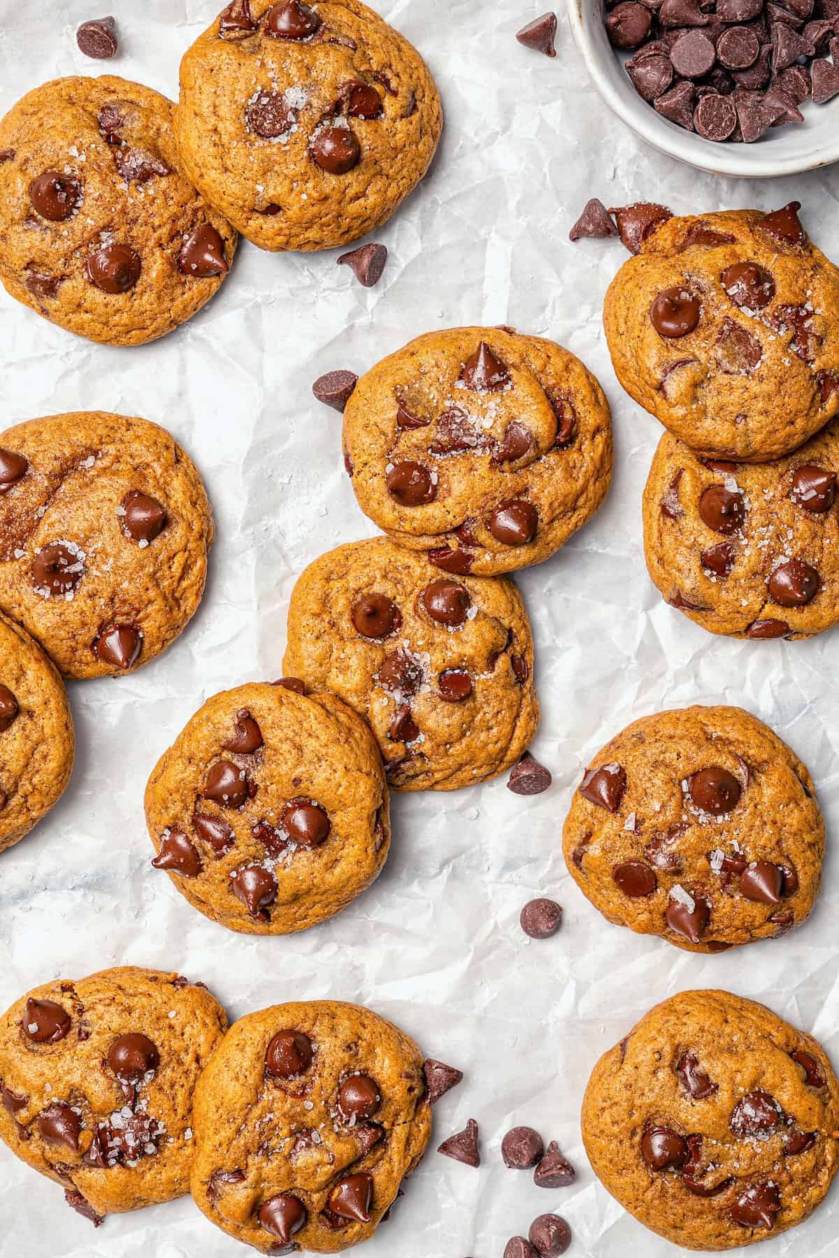 Soft, moist, and chewy, these Pumpkin Chocolate Chip Cookies are the perfect sweet treat for fall! Pumpkin pie spice adds warm, cozy flavor. Pumpkin chocolate chip cookies on parchment paper with chocolate chips.