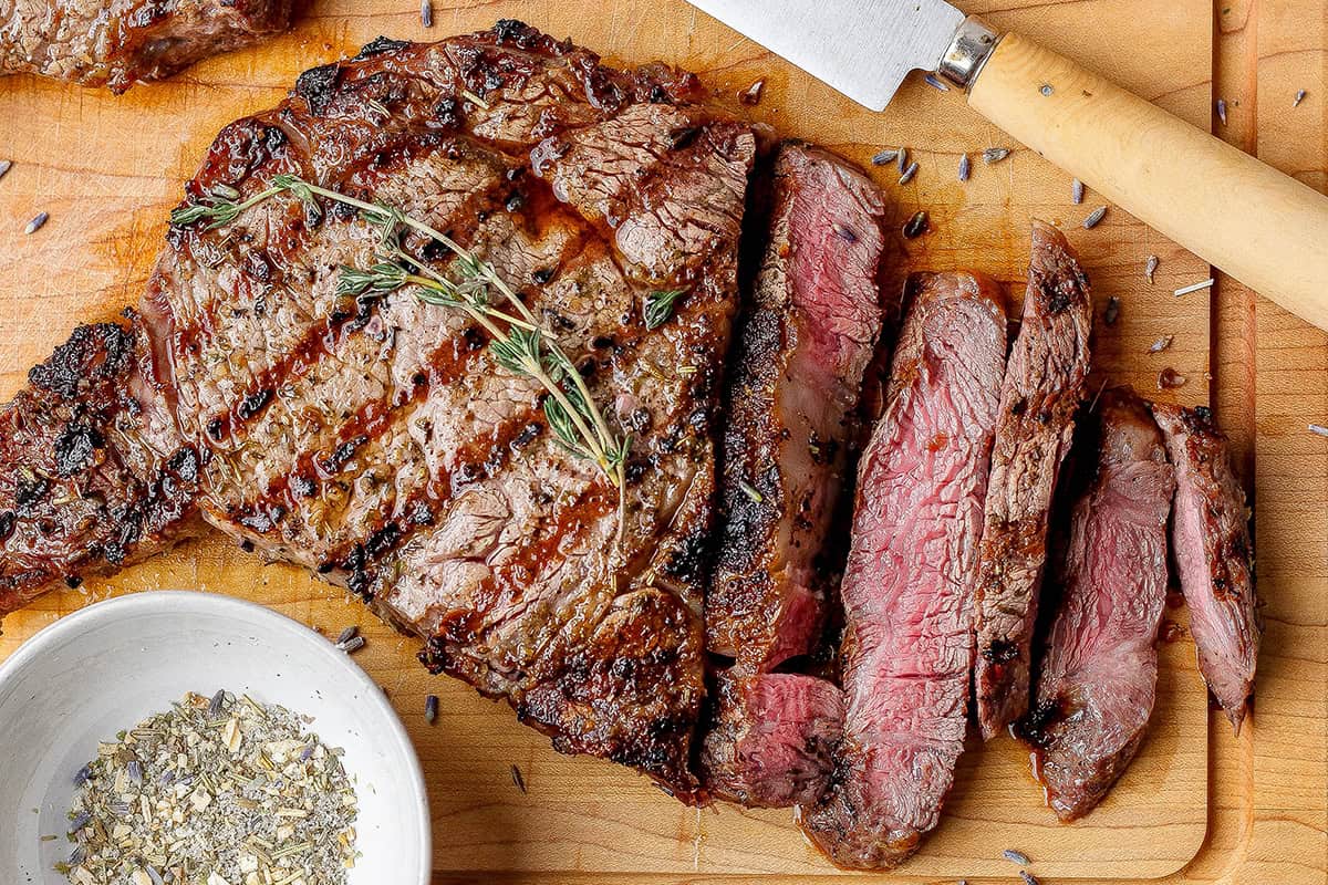 Sliced ribeye steak with bowl of steak seasoning.