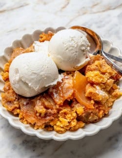 an individual serving of apple dump cake with scoops of vanilla ice cream, in a white dessert dish