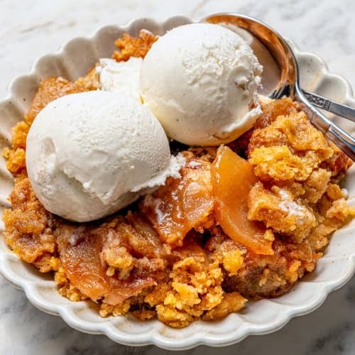 apple dump cake with scoops of vanilla ice cream, in a white dessert dish