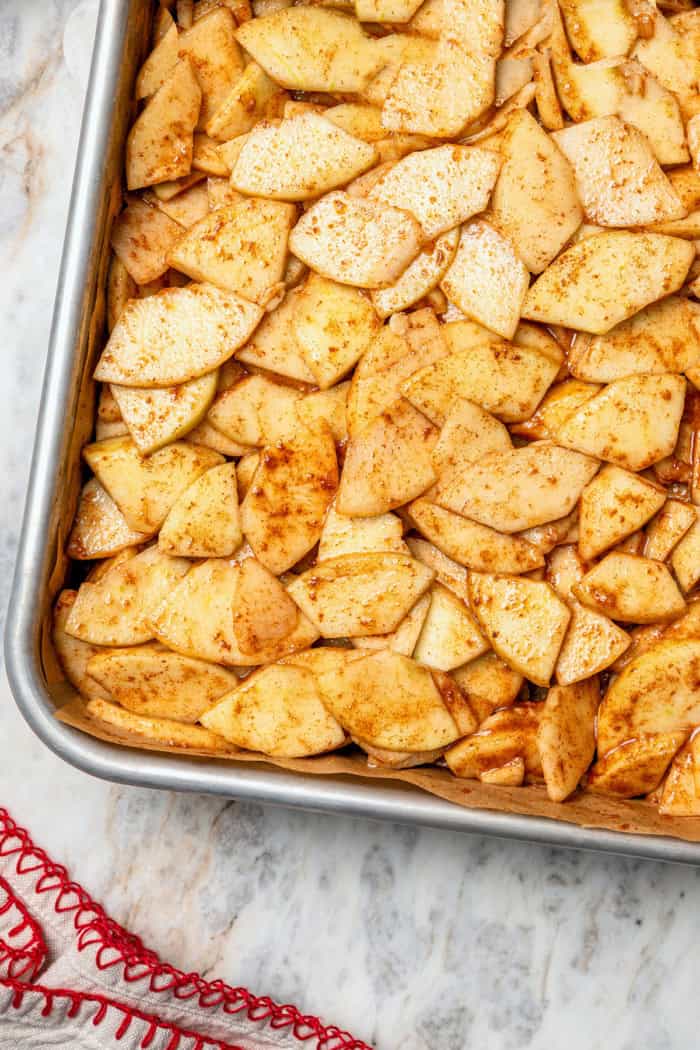 A brown sugar oat crumble mixture doubles as a crust and a topping for these easy Apple Pie Bars. The perfect fall treat for a crowd! sliced apples with apple pie spice in a baking pan