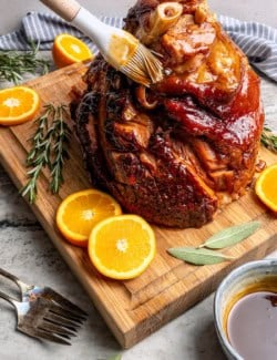 brushing a glaze over a cooked ham on a wood cutting board