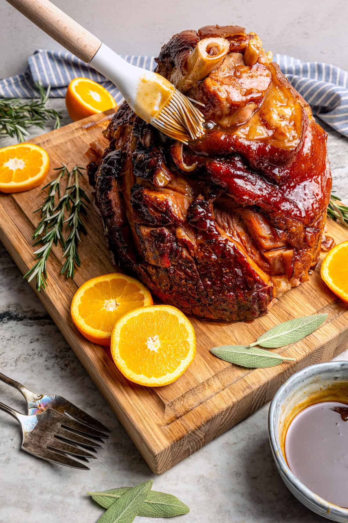 brushing a glaze over a cooked ham on a wood cutting board