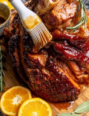 Brushing orange-brown sugar ham glaze onto ham.