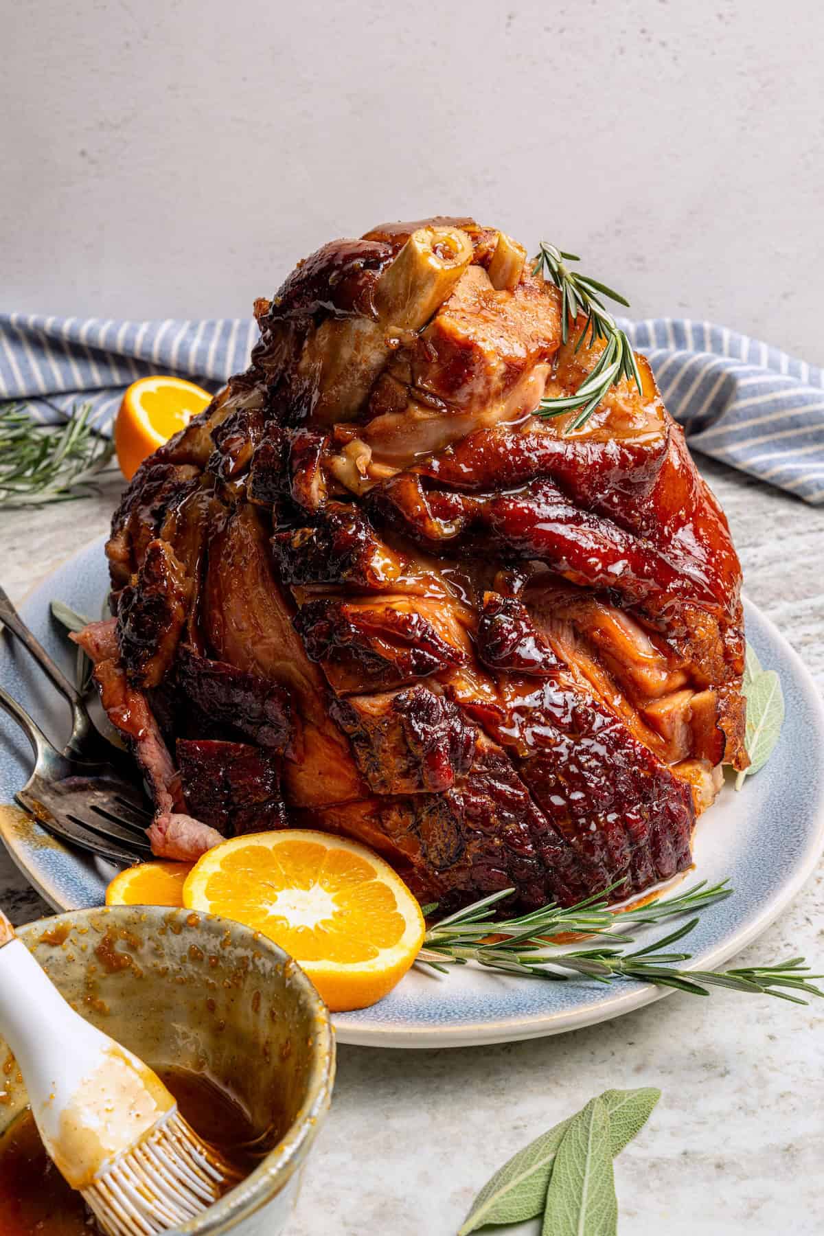 This Orange-Brown Sugar Ham Glaze is sweet and citrusy, but mustard, balsamic vinegar and warm spices add depth too. Easy and delicious! Platter with ham set next to bowl of orange-brown sugar ham glaze.