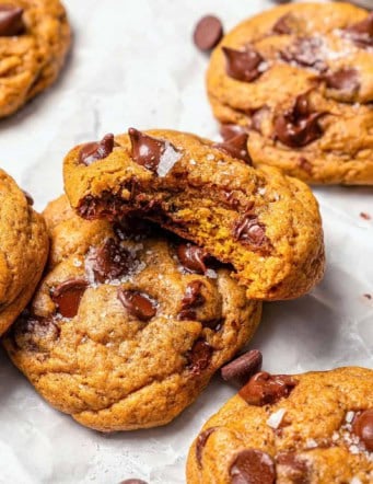 pumpkin chocolate chip cookies on white parchment paper, one with a bite out of it