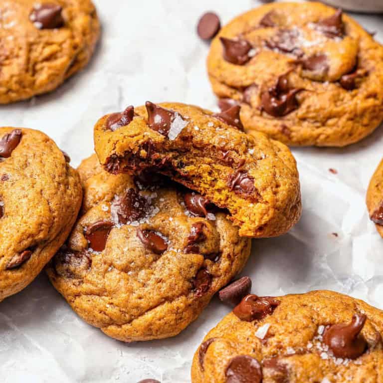 pumpkin chocolate chip cookies on white parchment paper, one with a bite out of it