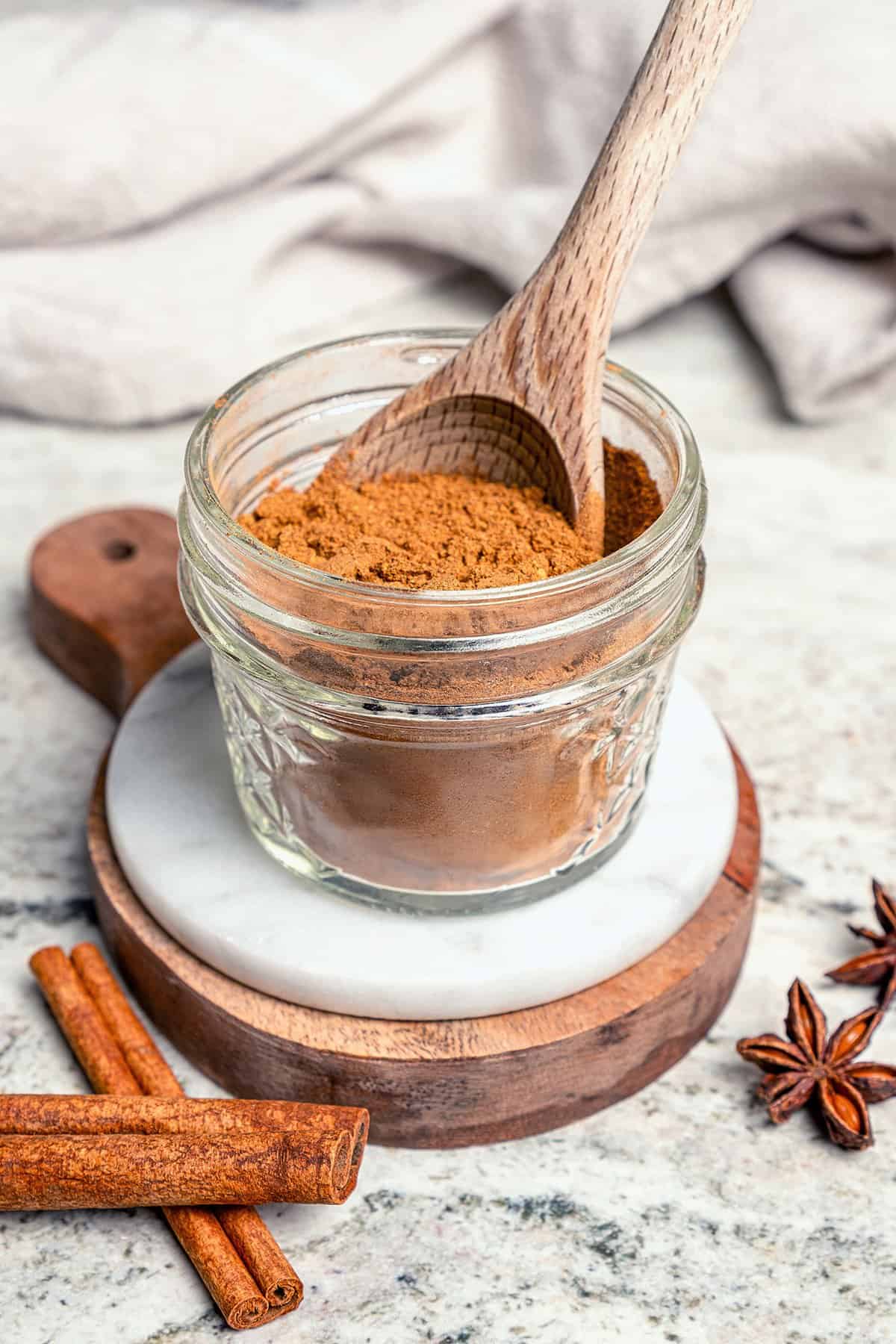 This isn't your ordinary homemade Pumpkin Pie Spice recipe! It’s rich and robust, with a touch of black pepper for some cozy warmth. a small jar of Pumpkin Pie Spice, with a wooden spoon in the jar