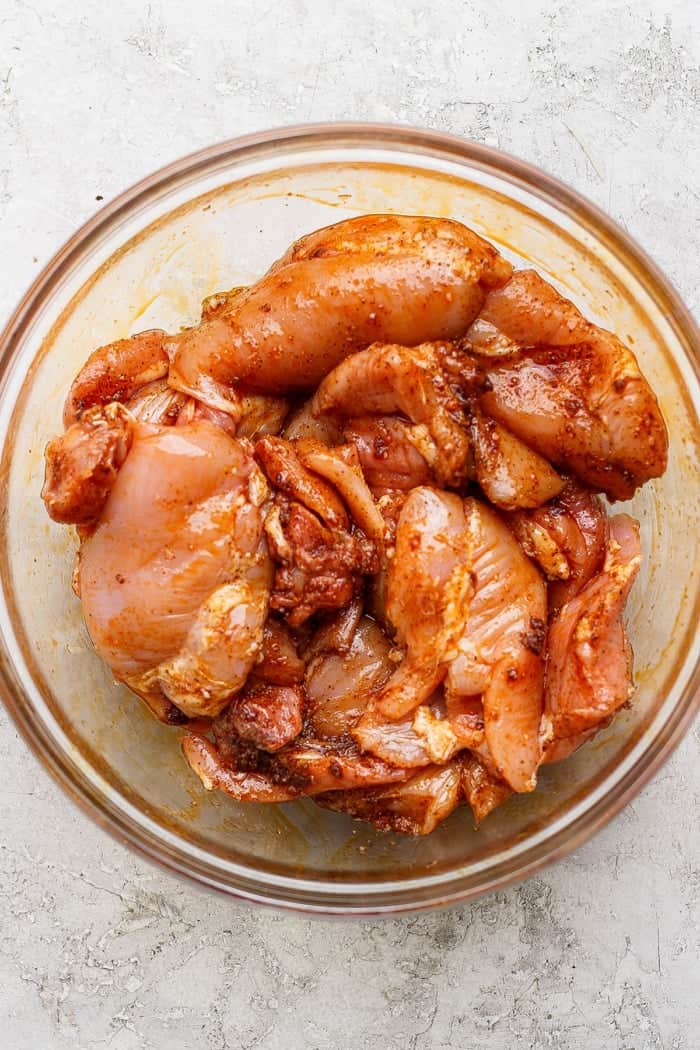 Chicken thighs in bowl with seasonings and oil.