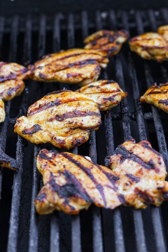 Boneless skinless chicken thighs cooking on grill.