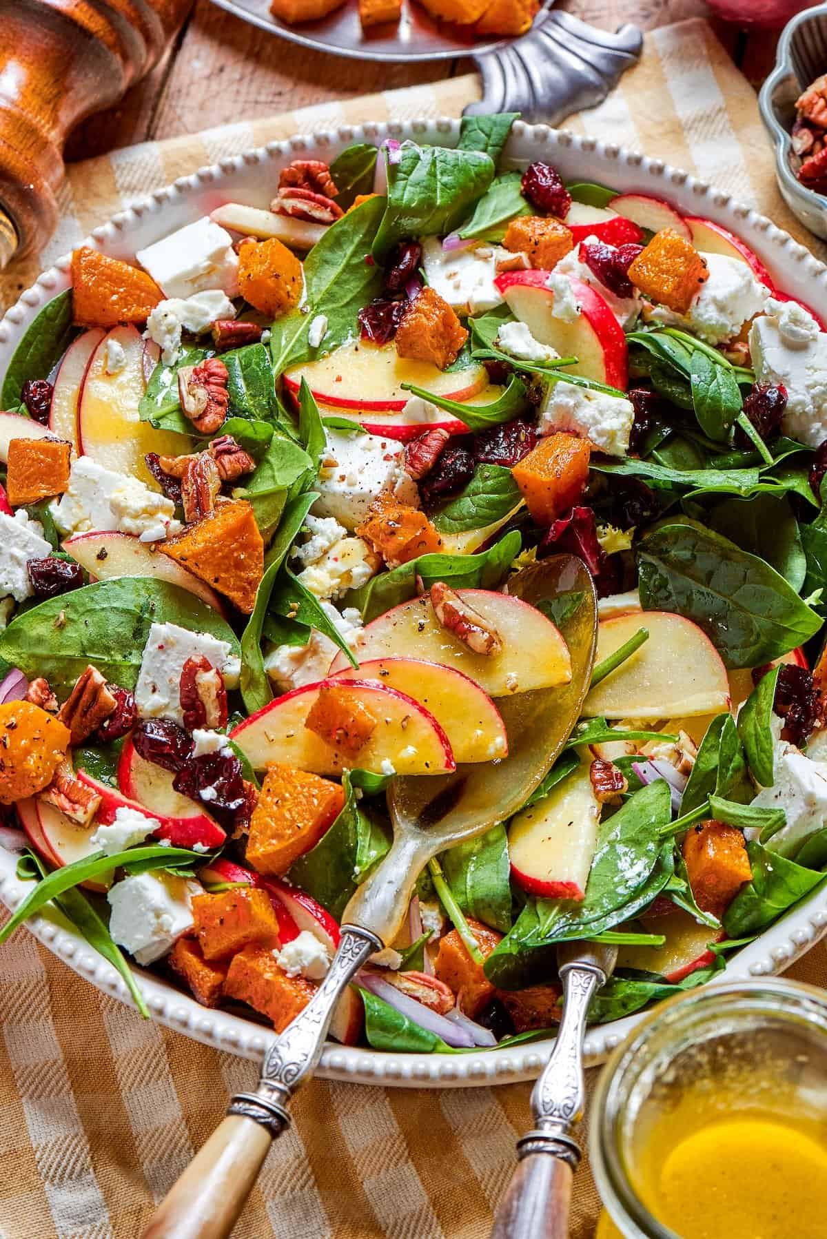 a platter of fall harvest salad with fresh greens, butternut squash, fresh greens, pecans, cranberries, and goat cheese