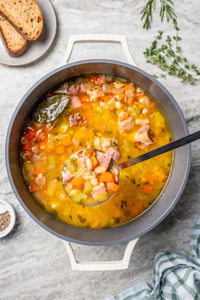 Ladle of ham and bean soup held over pot.