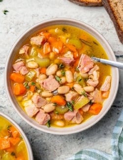 Spoon in bowl of ham and bean soup.
