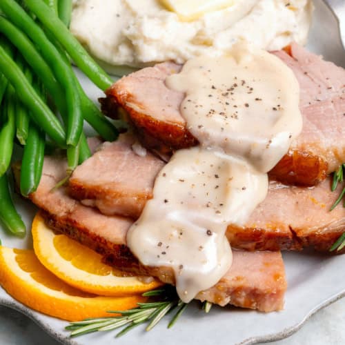 a plate of green beans, mashed potatoes, and sliced ham with ham gravy