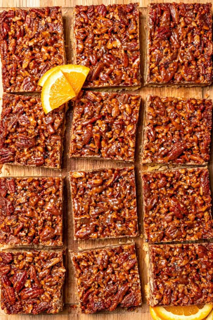 These Pecan Pie Bars have a caramel filling, buttery shortbread crust and NO corn syrup! Honey and brown sugar adds the perfect sweetness. Overhead view of sliced pecan pie bars on cutting board.