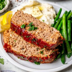 two slices of spicy meatloaf on a plate with mashed potatoes and green beans