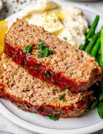 two slices of spicy meatloaf on a plate with mashed potatoes and green beans