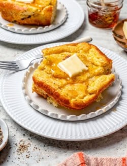 Spoon bread topped with honey and butter on white plate.