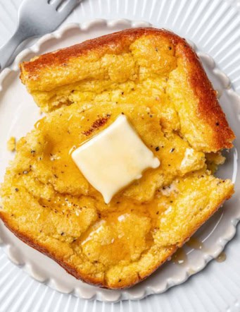 a white plate with a serving of spoon bread, with butter and honey on top