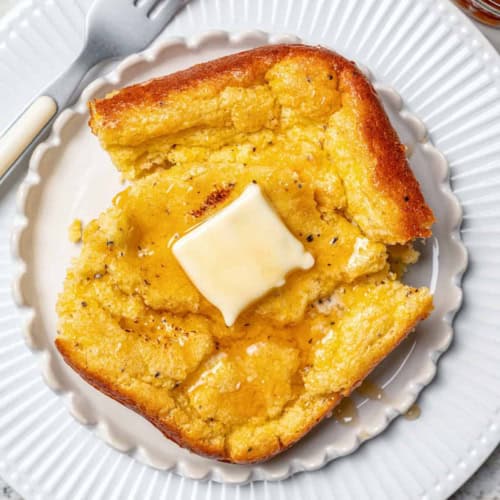 a white plate with a serving of spoon bread, with butter and honey on top