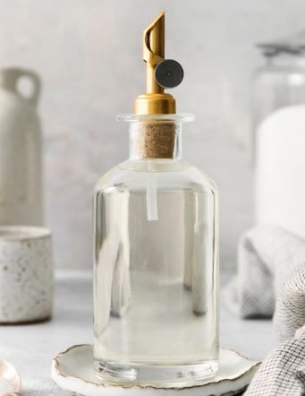 a clear bottle with a gold pour spout on top, full of simple syrup