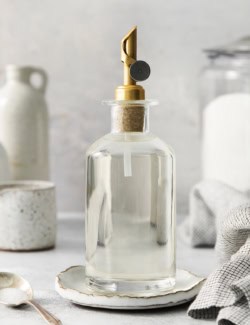 a clear bottle with a gold pour spout that has simple syrup in it