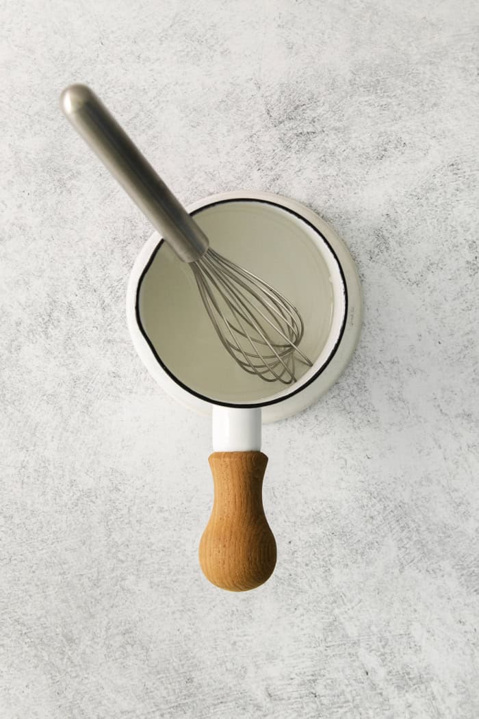 a whisk in a small white pan of simple syrup