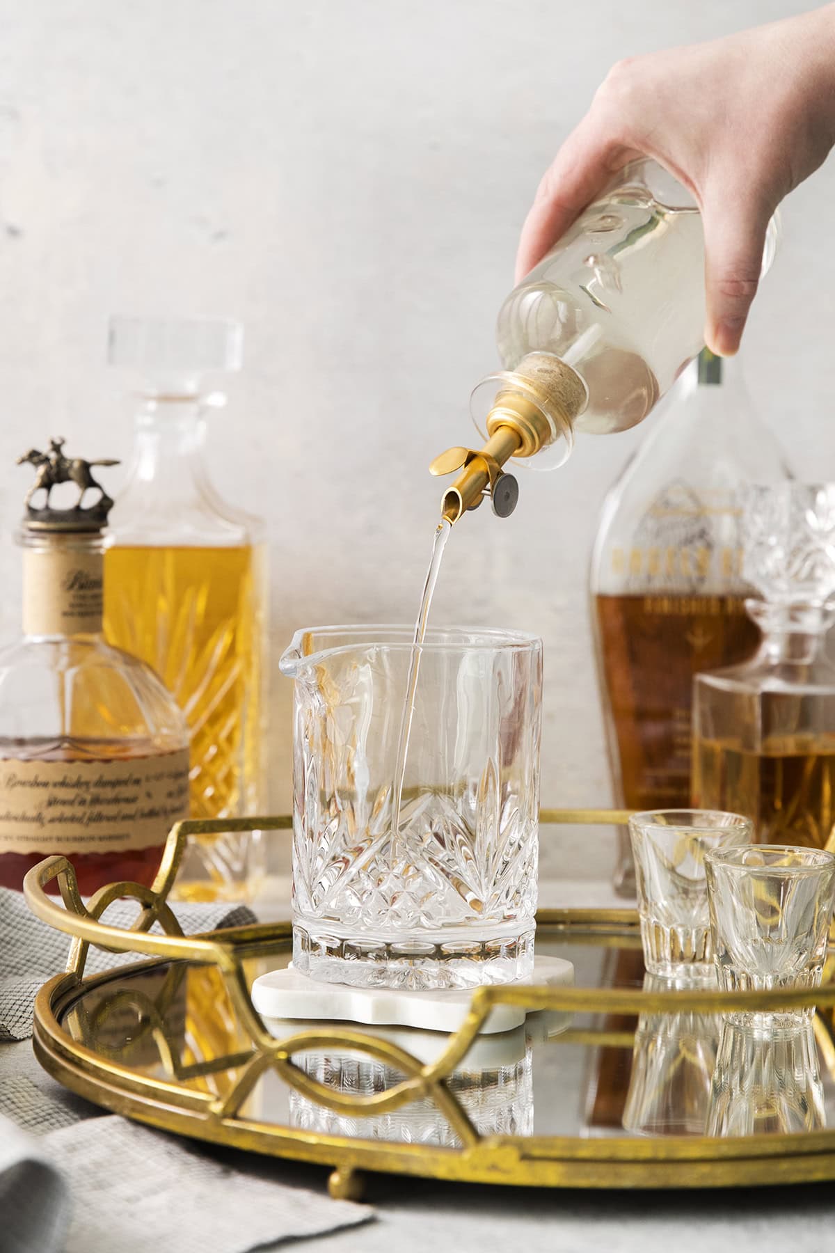 a hand pouring simple syrup from a clear bottle into a cocktail mixing glass