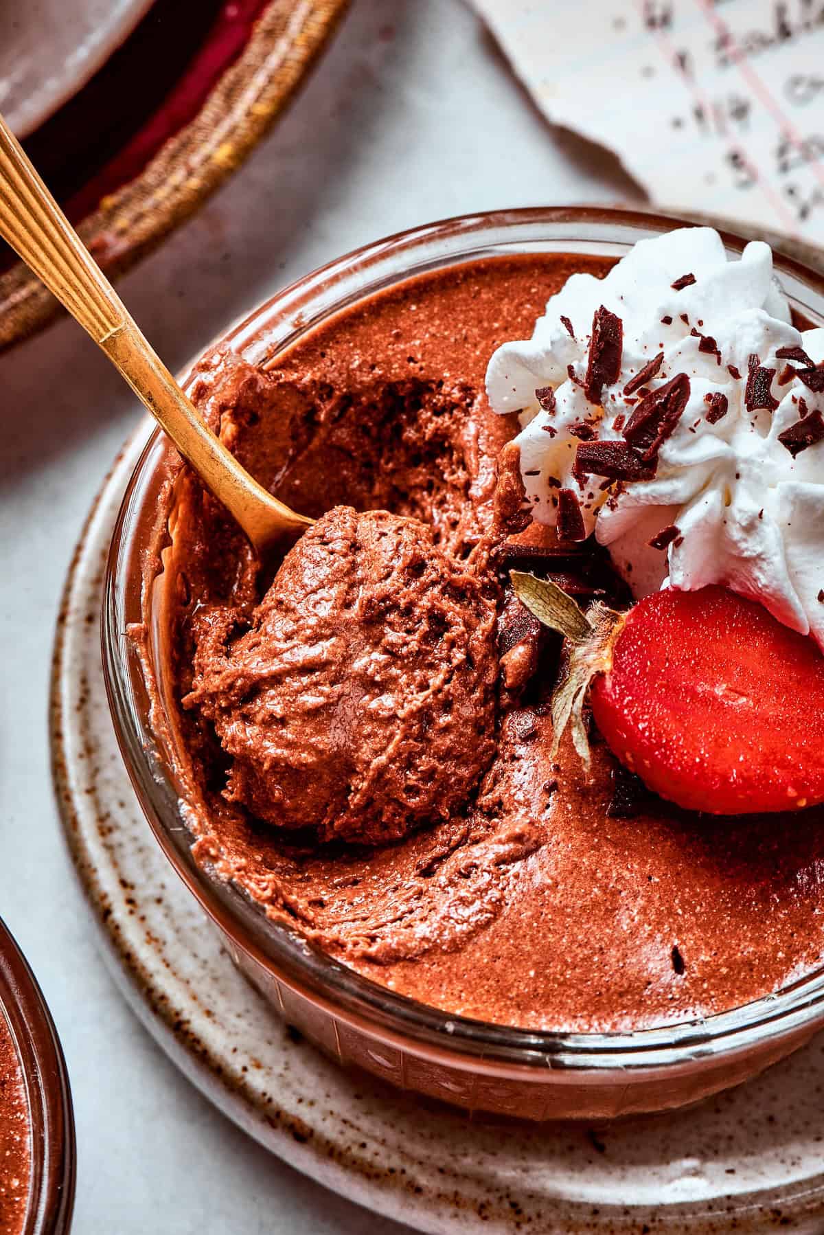 close-up photo of a cup of chocolate mousse with whipped cream and strawberries, with a spoon digging in