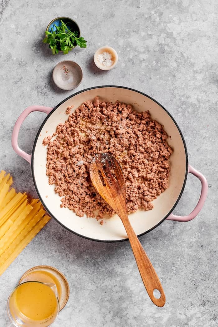 Ground beef in skillet with wooden spoon.