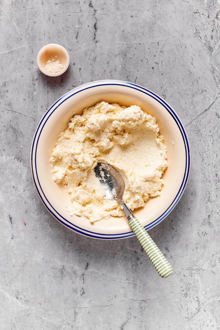 Ricotta and cheese mixture in bowl with spoon.
