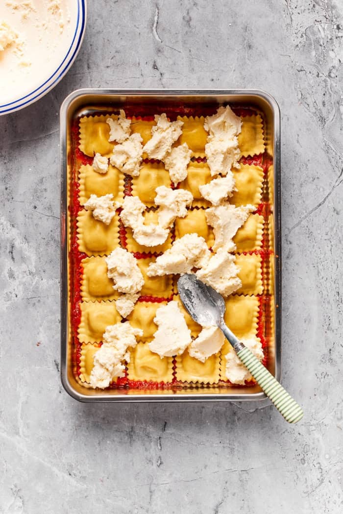 Spoon spreading ricotta mixture over ravioli.