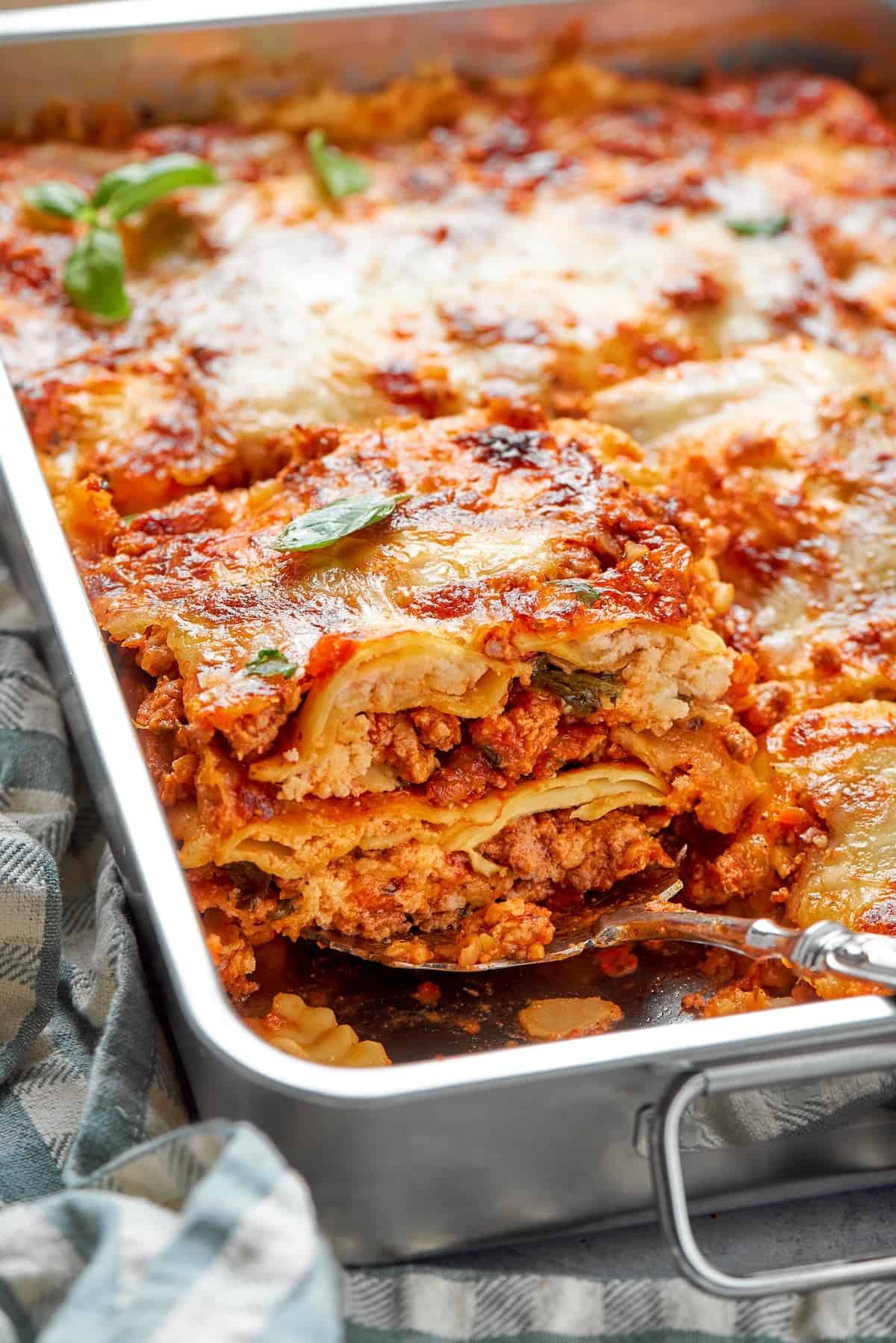 Serving spoon lifting portion of ravioli lasagna from pan.
