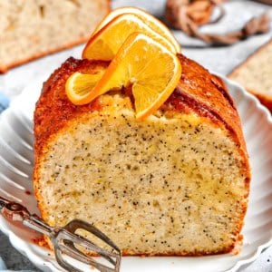 a loaf of orange poppy seed bread, sliced through the center, with fresh oranges slices on top