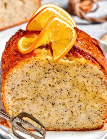 a loaf of orange poppy seed bread, sliced through the center, with fresh oranges slices on top