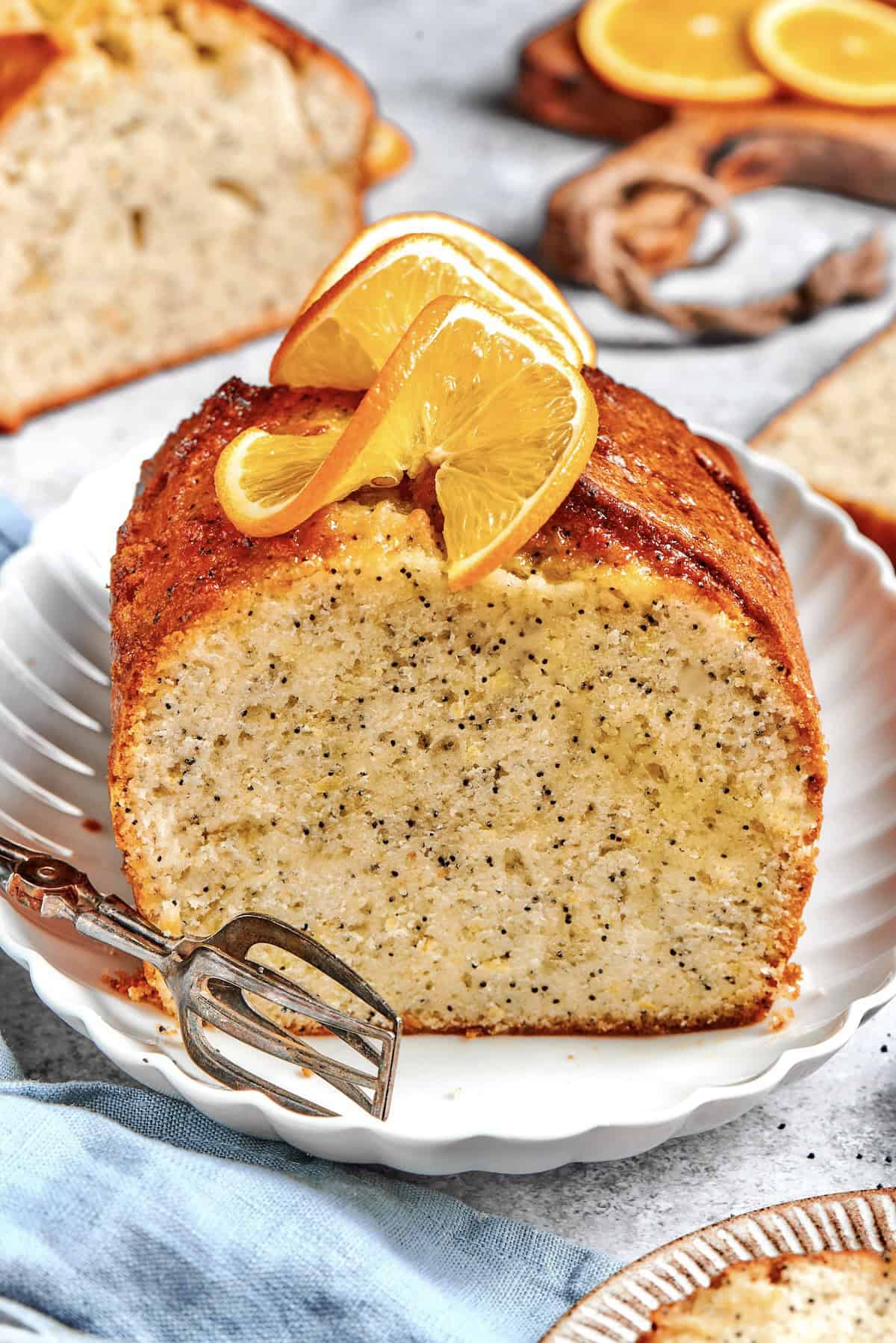 a loaf of orange poppy seed bread, sliced through the center, with fresh oranges slices on top