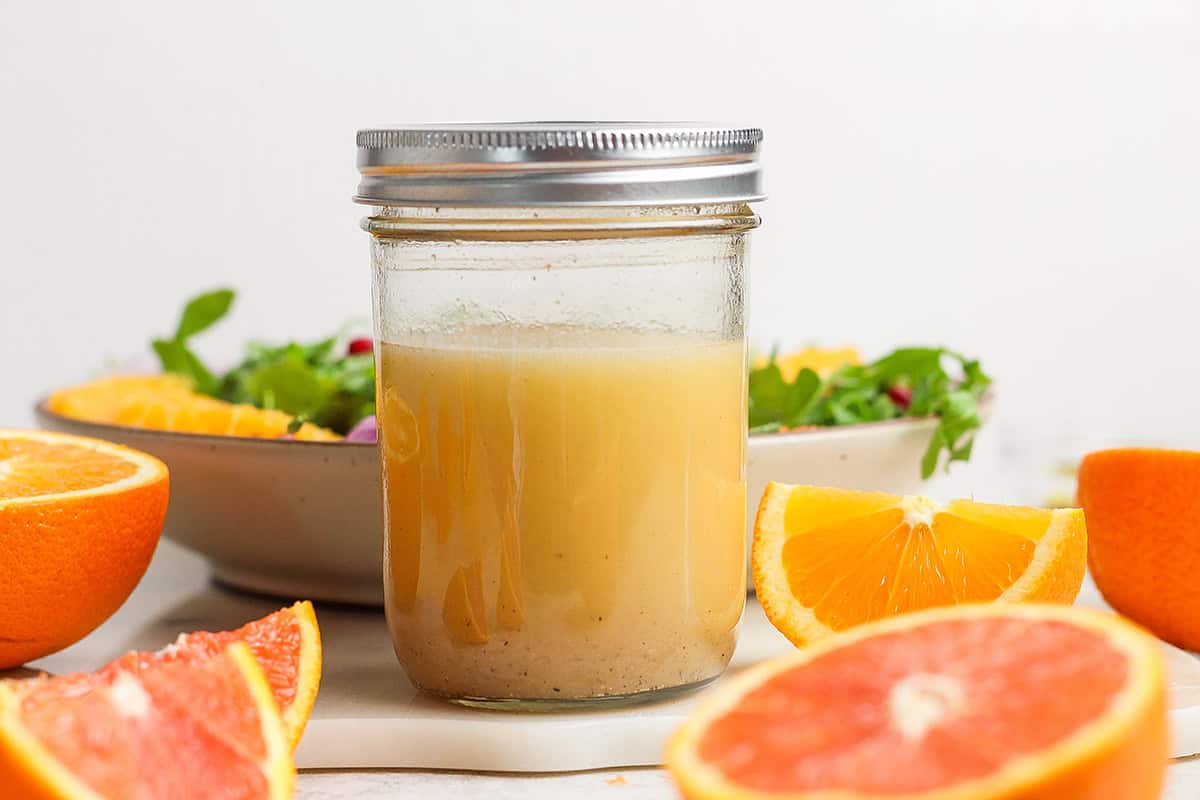 a small jar of citrus vinaigrette, with cut fresh citrus and a bowl of salad greens