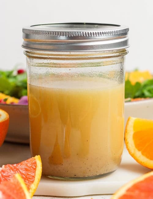 a jar of citrus vinaigrette, with cut fresh citrus and a bowl of salad greens