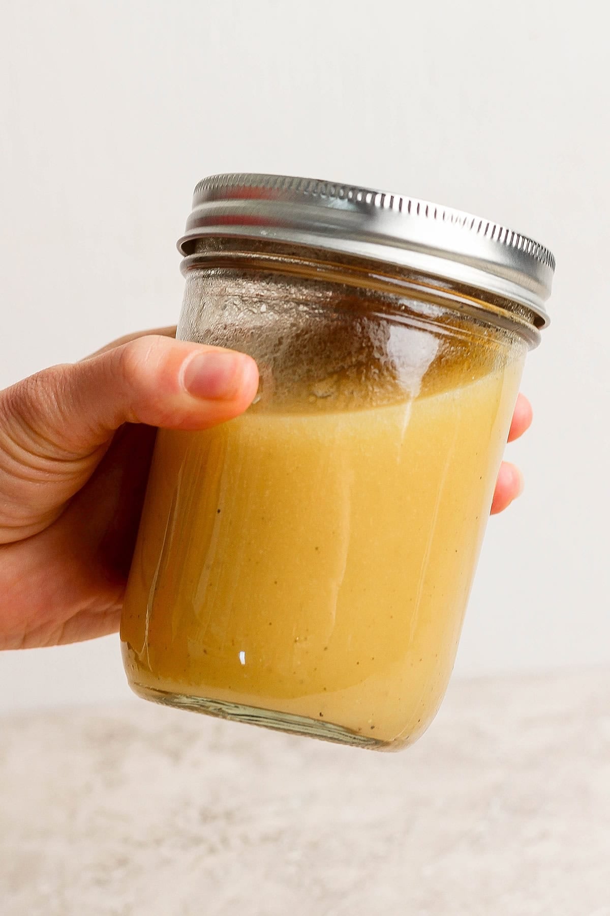 a hand shaking a jar of citrus salad dressing