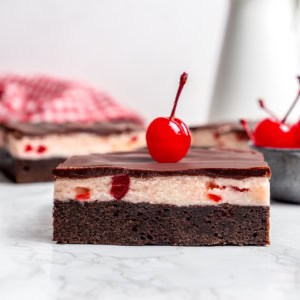side view of a cherry chocolate brownie with a maraschino cherry on top
