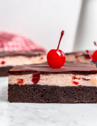 side view of a cherry chocolate brownie with a maraschino cherry on top