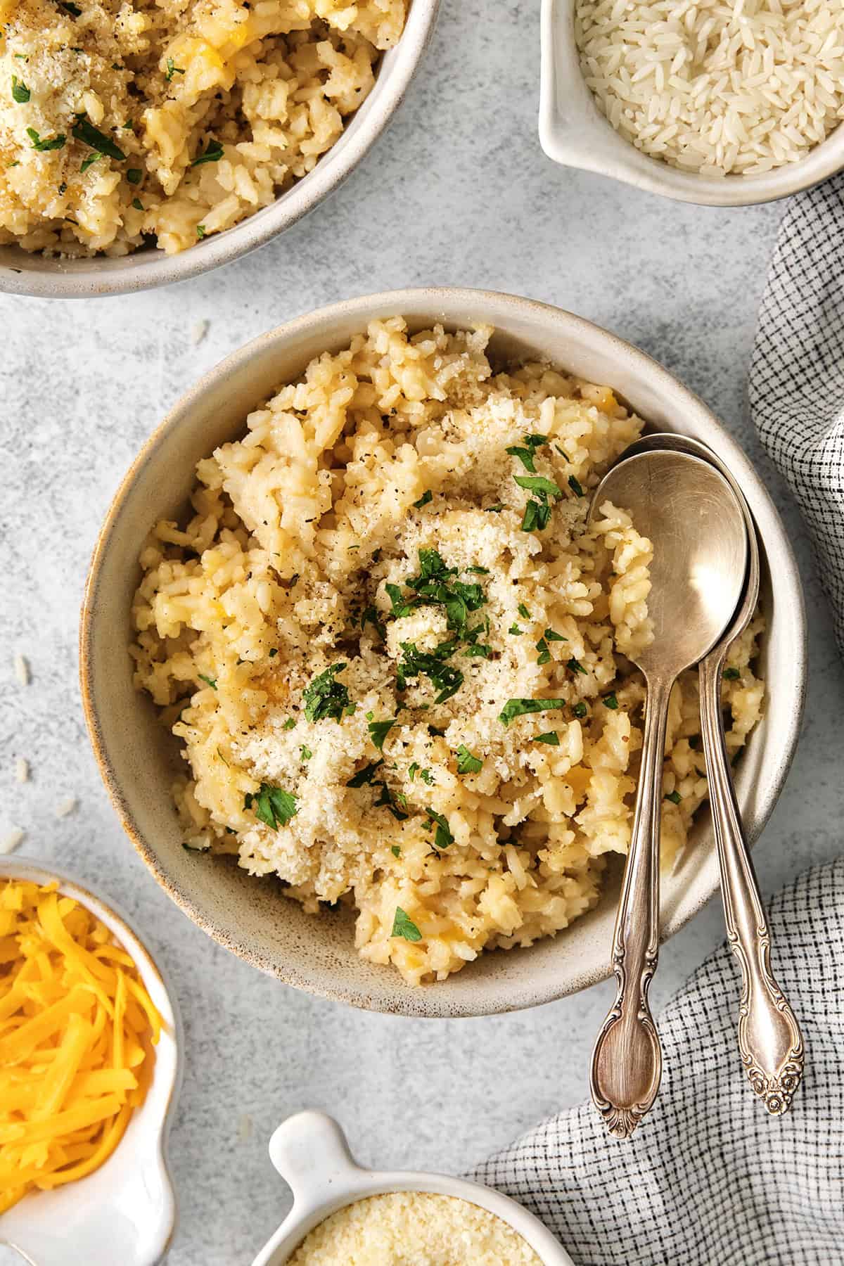 This creamy cheesy rice is made with cheddar and Parmesan for double the cheesy goodness. An easy side dish that pairs with any meal! Bowl of cheesy rice with two spoons.