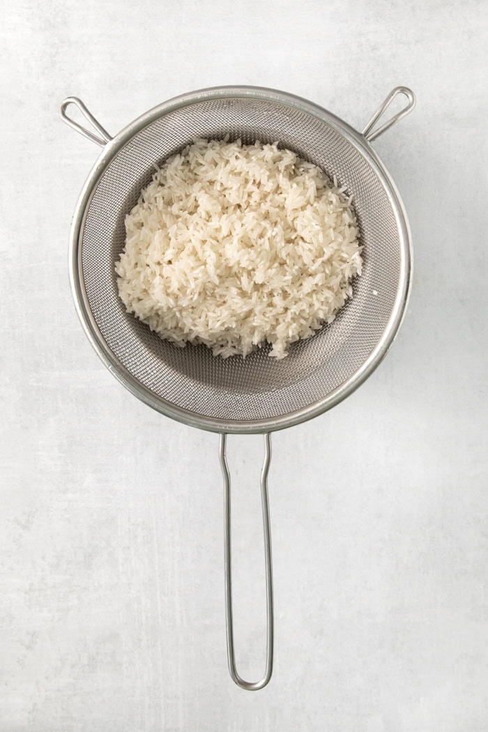 This creamy cheesy rice is made with cheddar and Parmesan for double the cheesy goodness. An easy side dish that pairs with any meal! Long grain white rice in colander.