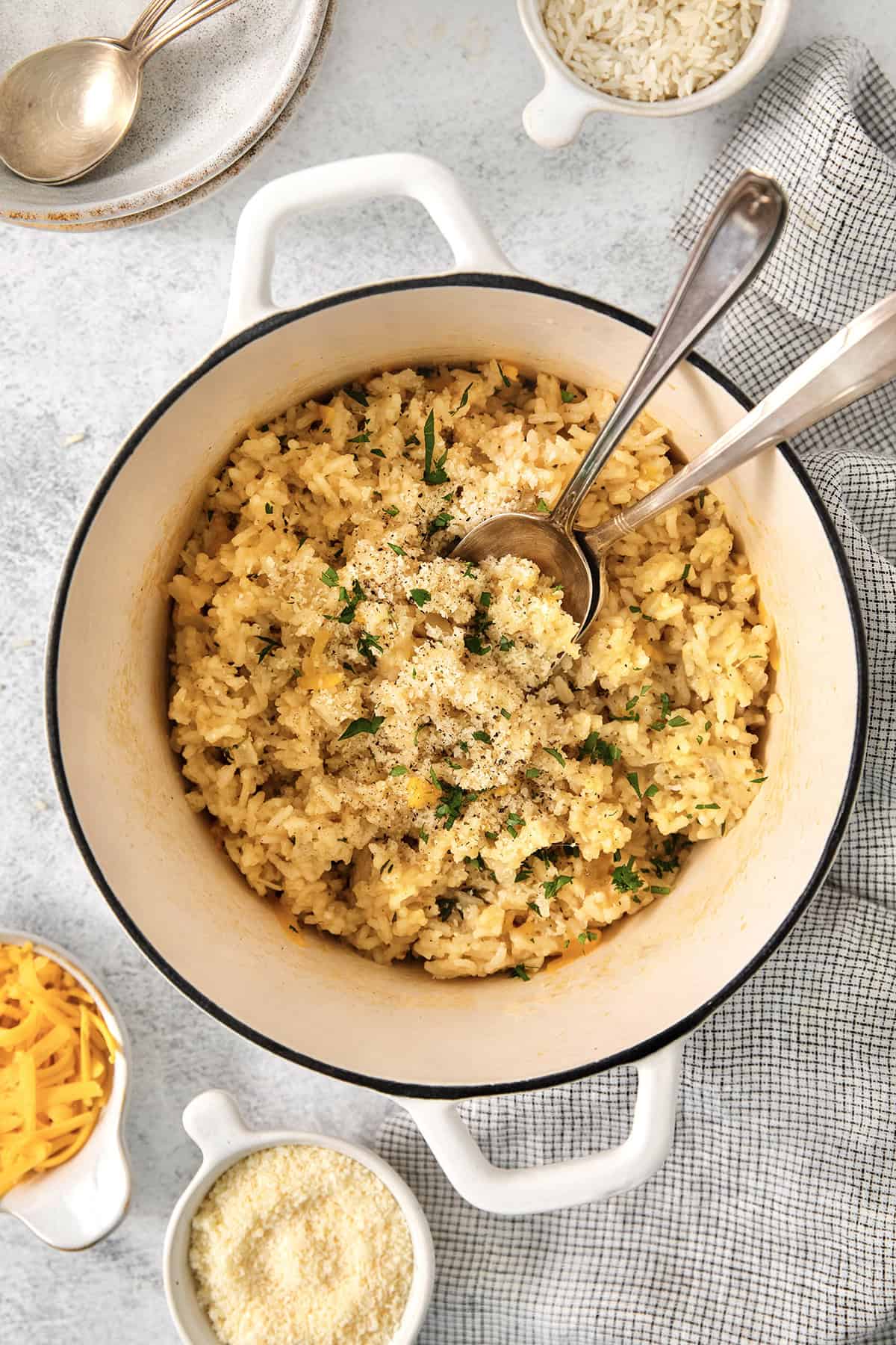 This creamy cheesy rice is made with cheddar and Parmesan for double the cheesy goodness. An easy side dish that pairs with any meal! Pot of cheesy rice set next to small bowls of cheddar and Parmesan.