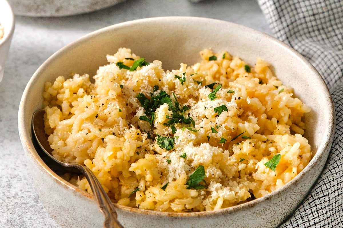This creamy cheesy rice is made with cheddar and Parmesan for double the cheesy goodness. An easy side dish that pairs with any meal! Spoon in bowl of cheesy rice.