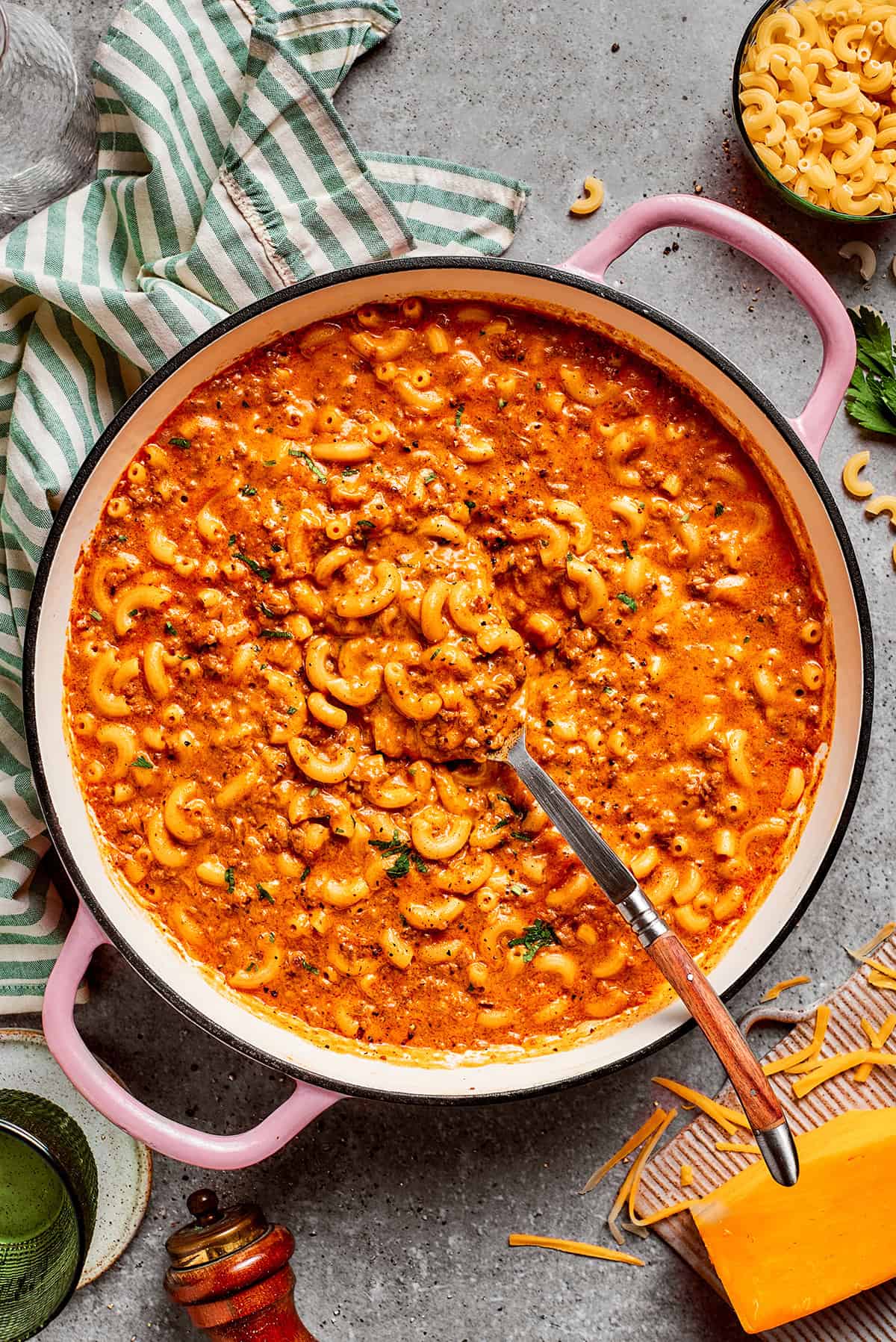 overhead photo of a pink pot of cheesy hamburger helper on a table with cheese and pasta