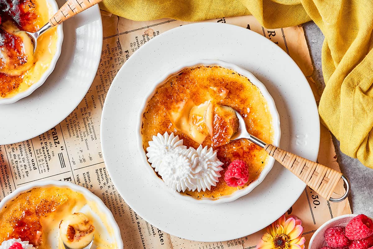 The silky custard in this Almond Vanilla Crème Brûlée lies beneath a glorious caramelized top. An elegant dessert that's surprisingly easy! overhead photo of white ramekins with creme brulee